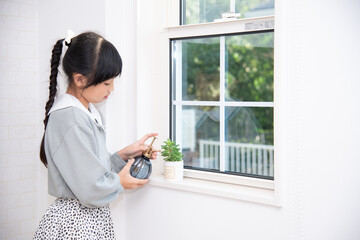 窓際に置いてある観葉植物に霧吹きをする小学生の女の子