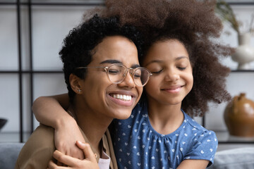 Head shot affectionate happy young African American woman in eyeglasses cuddling with adorable...