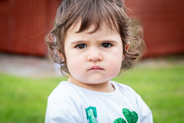 Young female toddler with big brown eyes and curly hair looking straight at the camera with an intense expression