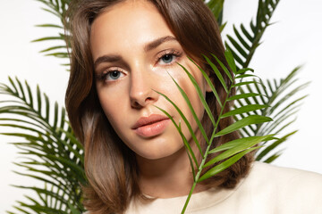 Naklejka premium Beautiful yong woman with perfect clean skin and natural make-up looking at camera with palm branch.