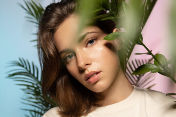 Naklejka premium Fashionable portrait of a beautiful girl with perfect skin on a colored background through tropical plants