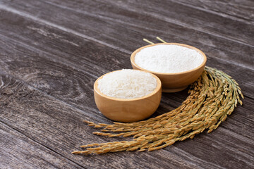 White jasmine rice and white rice flour in wooden bowl with paddy isolated on rustic wooden table background.