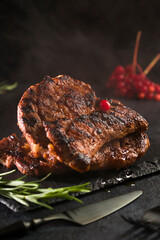 Hot steak with smoky meat grilled on a slate stone table. Black cutlery. Side view. Vertical position.