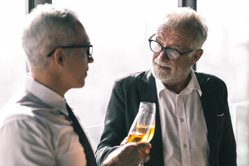 Picture of young business man talking to his older business partner. They are in white shirt and black tie. They are sitting on a table in a hotel lobby. 