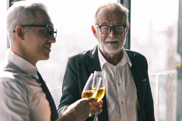 Picture of young business man talking to his older business partner. They are in white shirt and black tie. They are sitting on a table in a hotel lobby. 