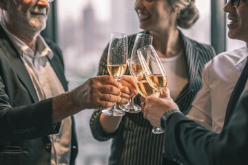 Picture of young business man and woman talking to his older business partner. They are in white shirt and black tie. They are sitting on a table in a hotel lobby. They are holding a champagne glass. 