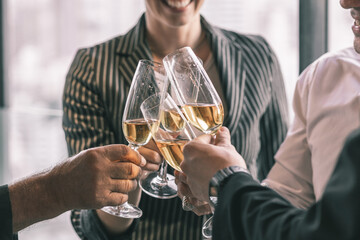 Picture of young business man and woman talking to his older business partner. They are in white shirt and black tie. They are sitting on a table in a hotel lobby. They are holding a champagne glass. 