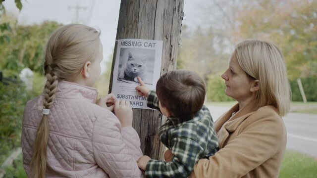 A woman with two children attaches a leaflet about a missing cat to a pole