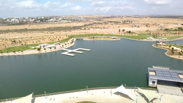 Flying forward over the artificial lake in the park with Beer Sheva buildings at background
