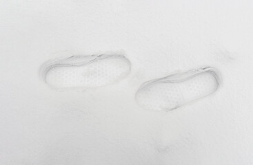Two prints of men's boots, toes pointing towards each other, on freshly fallen white snow.