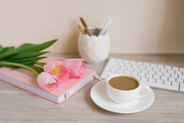 Home office workplace: cup of coffee, notebook, keyboard, tulip flowers, brushes, on wooden background background