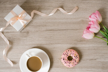 Cup of coffee, pink tulips on wooden background. Spring woman's day greetings. top view, flat lay, copy space.