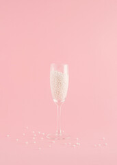 Creative Christmas arrangement made of a champagne glass with pearls on a pastel pink background. Minimal New Year concept. Party inspiration.