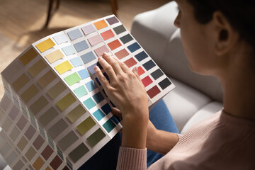 Close up woman homeowner choosing color from samples catalogue, preparing for house renovation concept, young female holding palette of wall paint colors, interior designer working on project