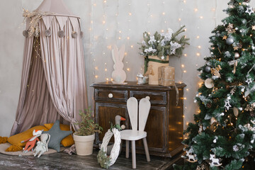 Christmas and New Year's decoration of the children's room for the holiday: a tree in a pot, a highchair in the form of a bunny, lights, pillows and toys. Bed awning and tree in the house