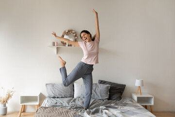 Overjoyed funny woman jumping on comfortable cozy bed at home, enjoying morning, starting new day,...