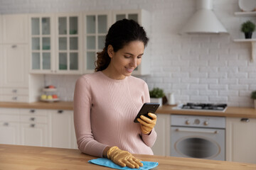 Smiling woman housewife using smartphone, distracted from cleaning, chatting online during break,...