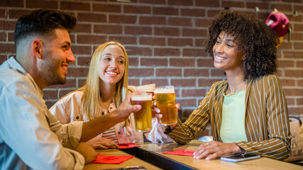 Group of friends cheering with beer and having fun in a pub, multicultural people haongout