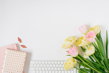 Keyboard on a white background with tulip flowers, notepads and earrings. Flat lay. Top view. The concept of a female freelancer's office.