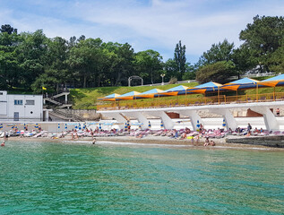 View of the pebble beach with people, sun loungers, umbrellas and an air solarium with a canopy,...
