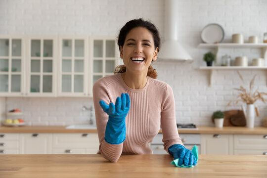 Head shot portrait excited woman in gloves cleaning wooden table at home, looking at camera, happy young female housewife blogger recording video tutorial in modern kitchen, housekeeping concept
