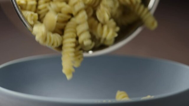 Slow motion pesto fusilli poured in blue bowl