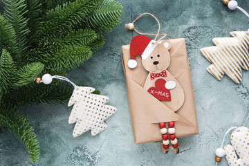 Gift decorated with a wooden bear in a santa claus hat with a heart in his paws with the text x-mas. Realistic artificial fir branch. White and gold Christmas decorations. Christmas card. Flat lay.
