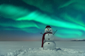 Funny snowman in stylish red hat and red scalf on snowy field against the backdrop of incredible...