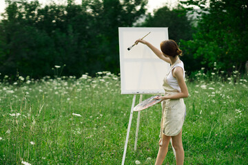 woman artist paints on easel in nature landscape