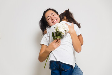 Girl child daughter hugging happy mom, congratulating with bouquet during Women's or Mother's Day. Copy space for ad