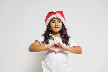 Smiling child girl in christmas santa hat showing heart gesture, congratulating with xmas holiday. Love, care and trust