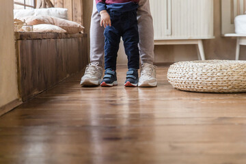Legs of parent, son standing at home on wood floor heating. Toddler's, adult feet on wooden...