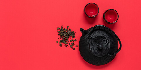 Black metal teapot and cups for tea on a red textured background. View from above. Asian tea...