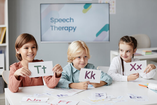 Group of children sitting at the table and showing cards with English alphabet during lesson at English school