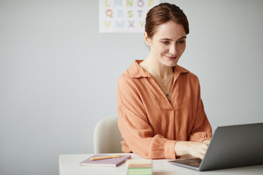 Young teacher sitting at her workplace and working online on laptop, she preparing for lessons at school