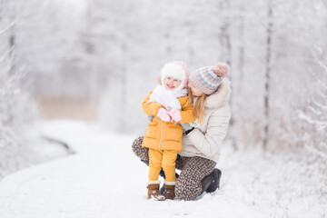 Happy young adult mother hugging and tickling little daughter on white snow covered trail at nature...