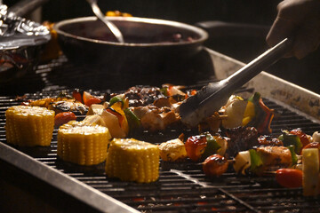 A chef prepared tasty beef steaks and skewers grilled on cast iron with fire for barbecue party camp and his reunion friends.