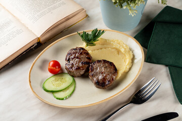 Mashed potato with roasted pork cutlets on a beautiful clay plate, light marble table background, restaurant setting
