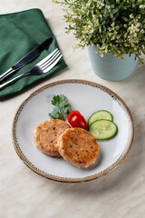 Two golden roasted salmon cutlets with two slices of cucumber and cherry tomatoes, top view with copy space
