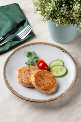 Salmon fritters with cucumber and cherry tomatoes, top view on light marble restaurant table, above view with copy space