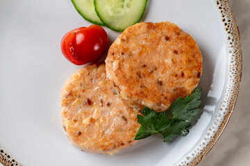 Two golden roasted salmon cutlets with two slices of cucumber and cherry tomatoes, top view with copy space