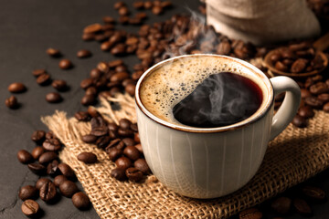 Cup of aromatic hot coffee and beans on black table, closeup