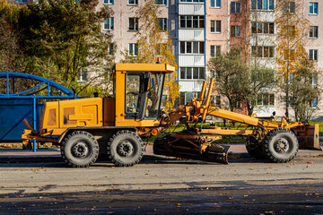 A grader performing road works in the center of a modern city. Road works in the fall.