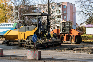 Fototapeta na wymiar An asphalt paving machine works in the city center in the fall. Repair of road surfaces in a modern city using specialized equipment.