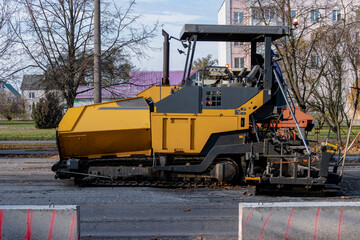An asphalt paving machine works in the city center in the fall. Repair of road surfaces in a modern city using specialized equipment.