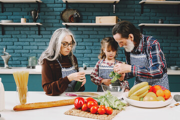 Senior grandparents couple with dgranddaughter cooking in kitchen