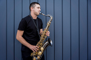 Fototapeta na wymiar Young street musician playing saxophone near the big blue wall
