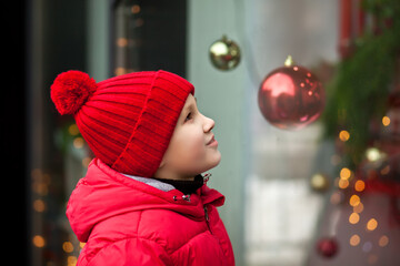 Adorable boy kid looking through the display window at Christmas decoration in the shop