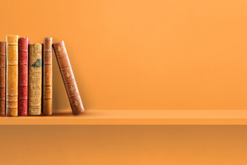 Row of old books on orange shelf. Horizontal background