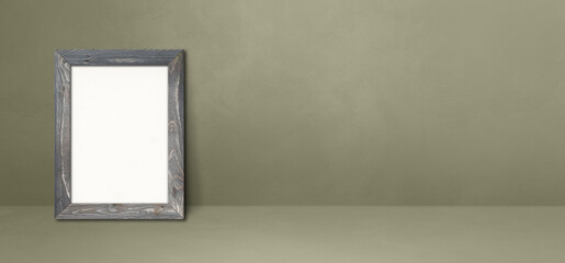 Wooden picture frame leaning on a grey wall. Horizontal banner